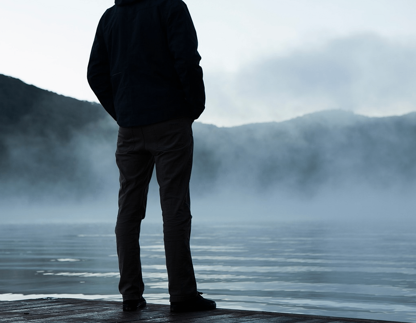 A man standing on a pier, looking out at the water